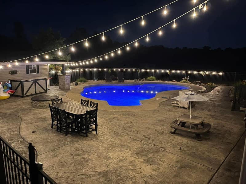 Stamped pool deck lit at night under string lights