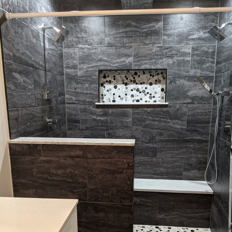 Walk-in shower with large charcoal tile, a pebble-tile niche and a half wall
